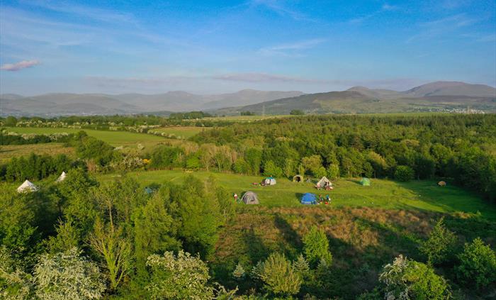 Birdseye view of the camping meadow, surrounded by trees and Eryri National Park in the distance